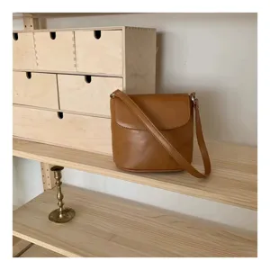 Detail view of a brown leather shoulder bag on a wooden shelf, minimalist aesthetic style.