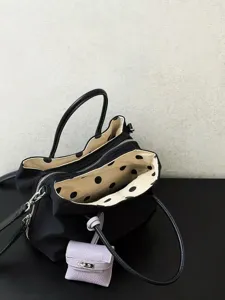 Black nylon tote bag interior detail showing cream polka dot lining and mini charm.
