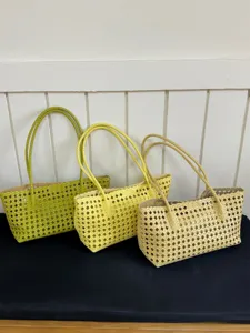 Detail view of three stylish hollow woven tote bags in lime, yellow and beige, perfect for summer.