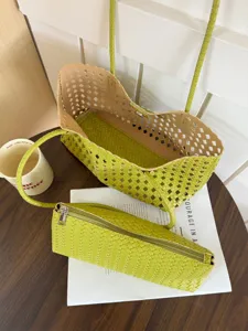 Detailed shot of green woven cutout shoulder bag and matching pouch on wooden table.