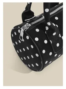 Close-up detail of black cylindrical handbag featuring white polka dots and silver zipper.