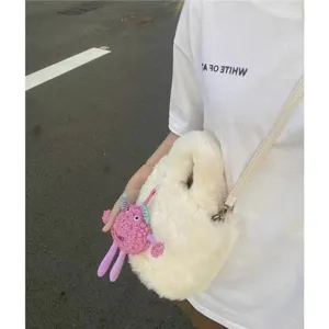 Detailed view of the white fluffy plush bucket bag with a cute pink monster pendant.