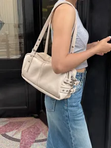 Detailed view of trendy beige shoulder bag, retro pillow bag style with chic metallic accents.