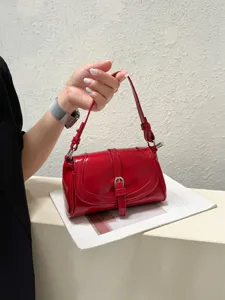 Close-up of red patent leather shoulder bag detail with elegant metal buckle and strap.