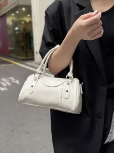 Close-up detail of white patent leather bowling handbag with metal rivets and sturdy double handles.