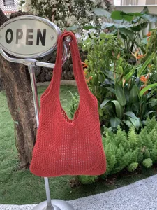 Close-up detail of the red knit hollow crochet shoulder bag in outdoor garden scene.