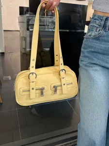 Yellow bowling shoulder bag detail shot, featuring dual straps, silver metal rings and zippers.