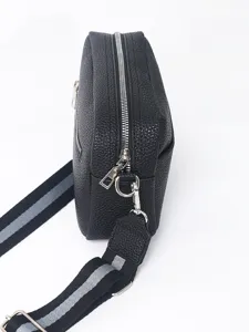 Detail close-up view of black PU leather crossbody bag zipper and striped strap texture details.