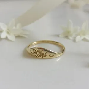 Gros plan d'une bague chevalière dorée avec de délicats motifs floraux gravés sur un fond blanc.