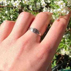 Gros plan de la bague chevalière florale gravée en argent portée au doigt avec des fleurs blanches.