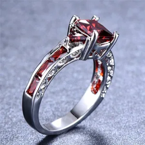 Détail de bague argentée pour femme avec un zircon rouge carré et des pierres.