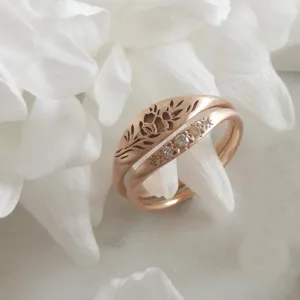 Gros plan détaillé de la bague florale ajourée en or rose et de son alliance de zircons.