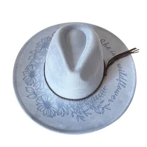 Detail view of light blue suede fedora hat with laser engraved daisies and wildflower text.