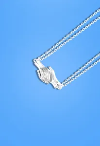 Close-up of magnetic couple hands pendant necklace with silver chain and clean blue background.