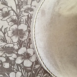 Gedetailleerde close-up van de suède cowboyhoed met gelaserde botanische bloemenprint.