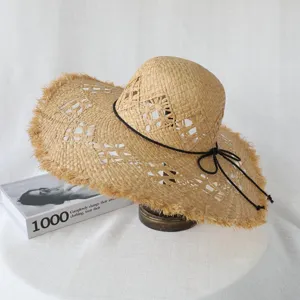 Close up of raffia straw sun hat with frayed edge and black drawstring detail for beach.
