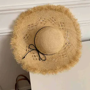 Detailed view of a handmade hollow raffia sun hat with delicate frayed edges and a black ribbon.