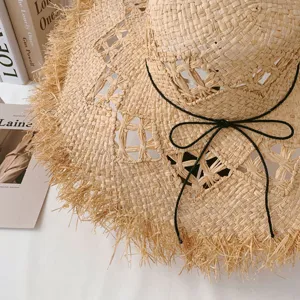 Close-up of french hollow raffia straw hat detail, frayed wide brim with black ribbon bow.