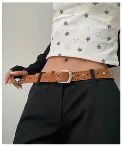 Gros plan détaillé d'une ceinture en cuir verni marron avec strass et découpes en cœur.