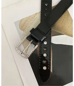 Détail de ceinture en cuir noir strassé avec boucle en cristal, découpes cœur et accessoires élégants.
