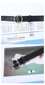 Close-up detail of black leather belt featuring metallic round buckle and pearl charm.
