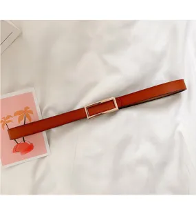 Detailed view of minimal brown leather belt with rectangular gold buckle on white fabric.