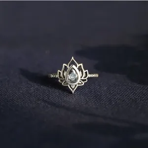 Dettaglio di un anello a goccia con fiore di loto in lega metallica e pietre splendenti.