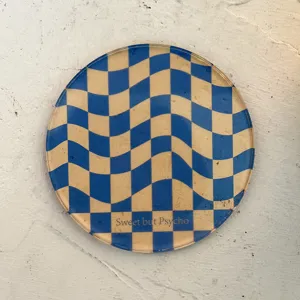 Round acrylic drink coaster detail shot with retro blue beige wavy checkerboard pattern.