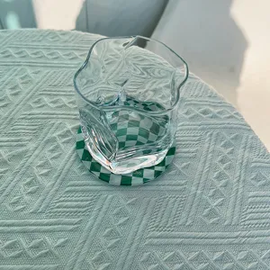Transparent irregular glass cup with green checkered coaster in minimalist cafe style.