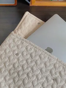 Nahaufnahme einer weichen, gesteppten Laptoptasche in Beige mit niedlichem Herzmuster.