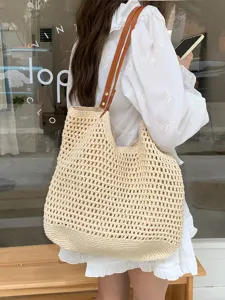 Dettaglio di una borsa tote in paglia intrecciata beige con manici in pelle marrone estiva.