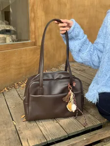 Nahaufnahme des braunen PU-Leder-Umhängetaschendetails mit Textur und Baseball-Anhänger.
