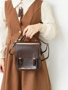 Détail de mini sac à dos rétro en similicuir marron avec double boucles et pièces métalliques.