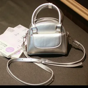Silver dome handbag detail view, showing sleek faux leather texture and dual zip closure.