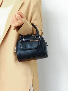 Detailed view of the black top handle mini shell bag, front pocket and metal hardware accent.