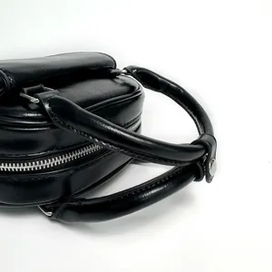 Black leather handbag detail view showcasing dual handles and metallic zipper hardware.