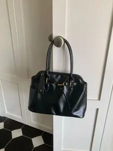 Black leather commuter handbag detail featuring elegant metallic hardware and classic strap design.