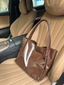 Brown glossy PU leather tote bag detail, featuring chain strap and heart pendant design.