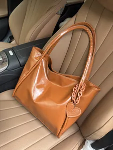 Brown glossy soft leather tote bag detail showcasing the stylish heart pendant and chain.