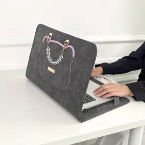 Detailaufnahme der grauen Laptoptasche mit süßem Bären-Design und Perlenkette am Tisch.