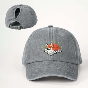 Primer plano del bordado del zorro durmiendo y del práctico ojal para coleta en la gorra vaquera.