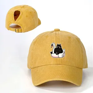 Vista detallada de la gorra de béisbol amarilla con coleta y estampado de gato negro y cisne.