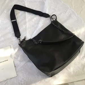 Close-up detail of black leather shoulder bag with wide strap and dark chain decoration.
