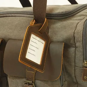 Leather luggage tag detail showing retro cowhide card holder on canvas travel duffel bag.