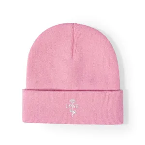 Gros plan détaillé du bonnet en tricot rose avec une fine broderie de rose blanche et texte.