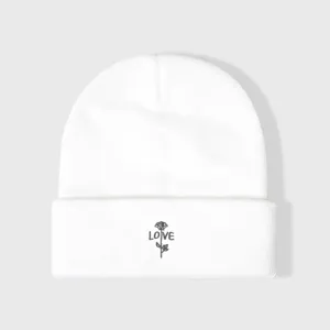 Détail de bonnet tricoté blanc, rose brodée et texte love, gros plan de bonnet d'hiver chaud.