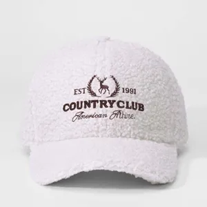 Détail d'une casquette de baseball en polaire teddy blanche avec logo cerf brodé et motif texte.