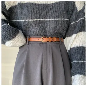 Primo piano dettagliato di una sottile cintura in pelle marrone con pantaloni e maglione.