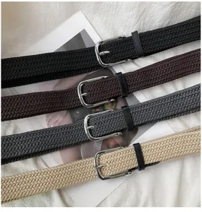 Detail view of woven elastic belts in black, brown, grey, and khaki with metal pin buckles.