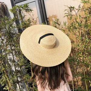 Chapeau de paille à très large bord style Hepburn avec dessus plat et ruban noir élégant.